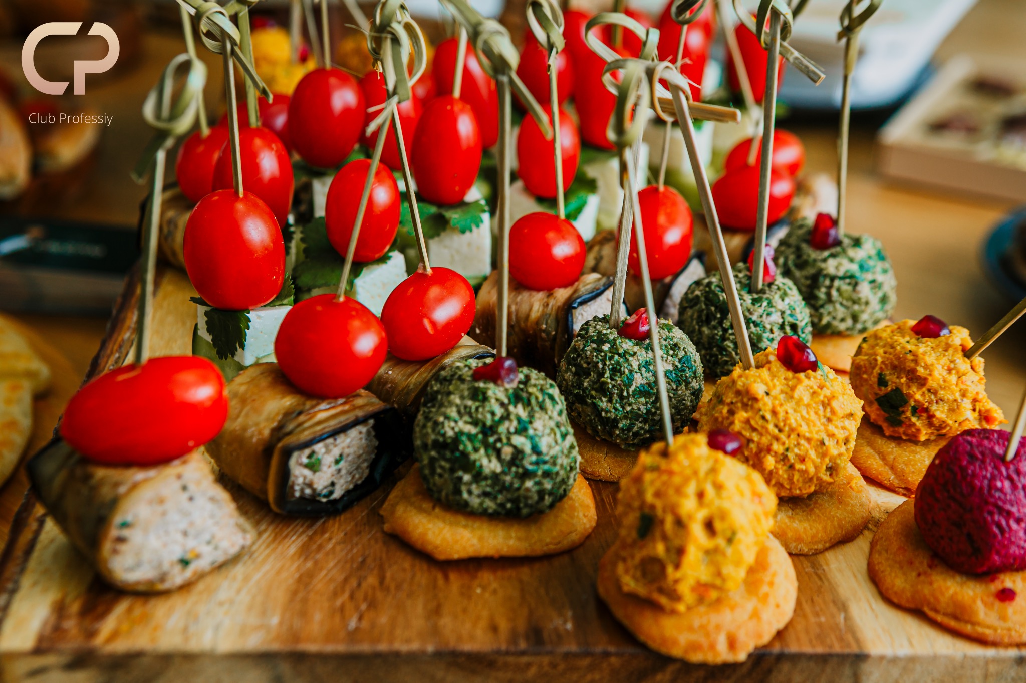 Eleganckie przekąski cateringowe: koreczki z pomidorkami cherry, roladki z bakłażana i kolorowe kulki na krakersach, ułożone na drewnianej desce.