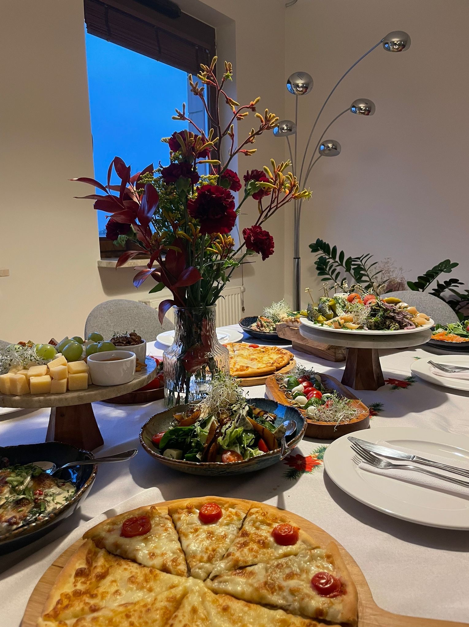 Stół cateringowy z gruzińskimi przekąskami: chaczapuri, sałatki, sery, kiszonki. Dekoracja kwiatowa i nowoczesna lampa. Idealne na spotkania i eventy.