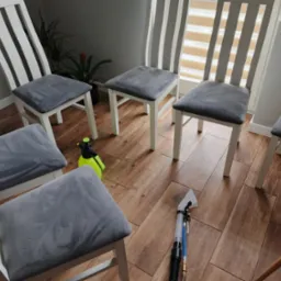 Krzesła z szarą tapicerką po praniu, widoczny spryskiwacz i odkurzacz piorący na drewnianej podłodze. Białe krzesła w jasnym pomieszczeniu.