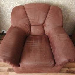 Ozontap Łukasz Kalita - Brązowy, pluszowy fotel po praniu tapicerki, widoczne jaśniejsze smugi po czyszczeniu. Na podłodze panele, w tle ściana z wzorzystą tapetą.