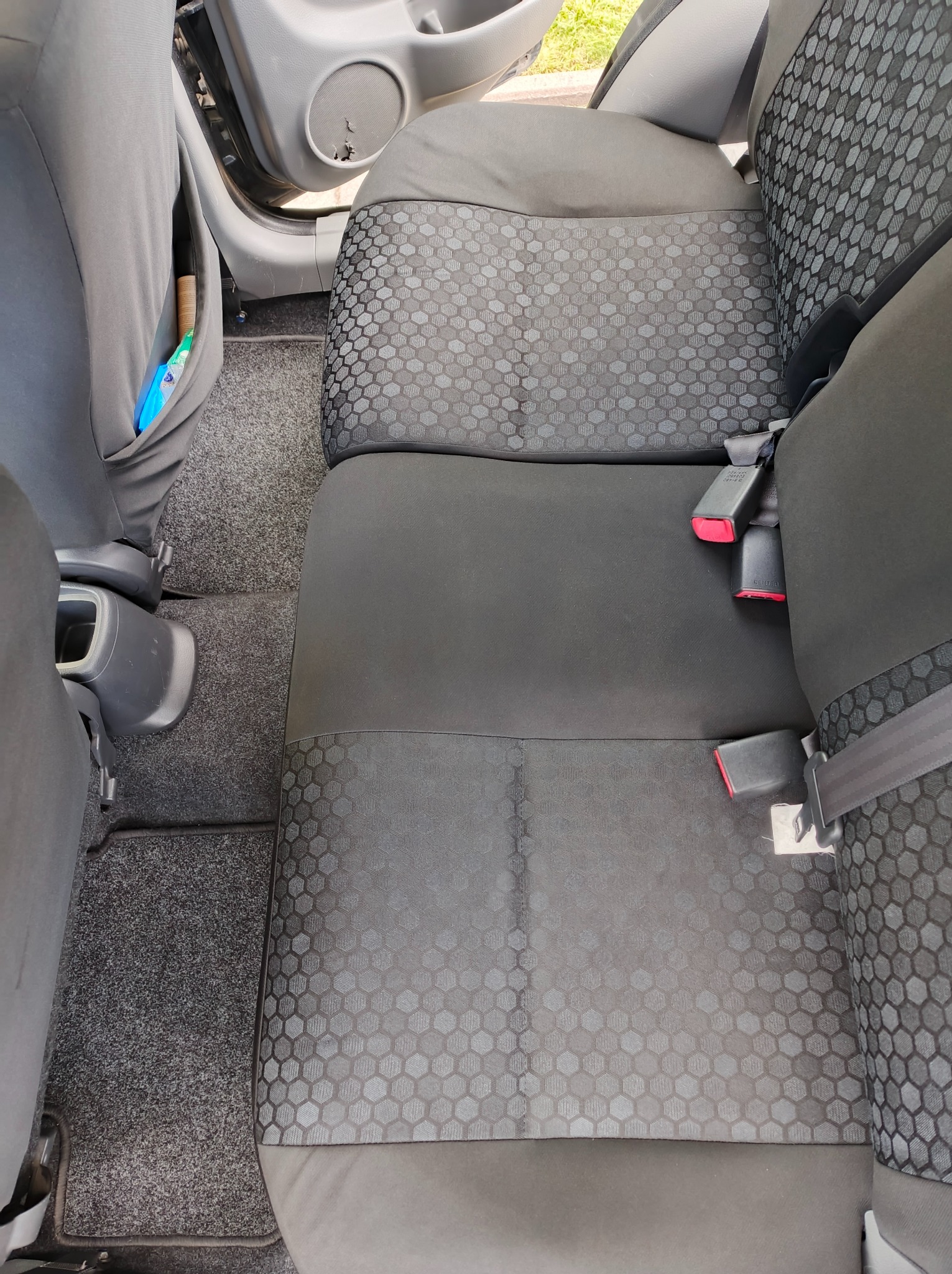 Wnętrze samochodu: tylna kanapa z szarą tapicerką w geometryczny wzór, pasy bezpieczeństwa, dywaniki i kieszeń na drobiazgi w oparciu fotela.
