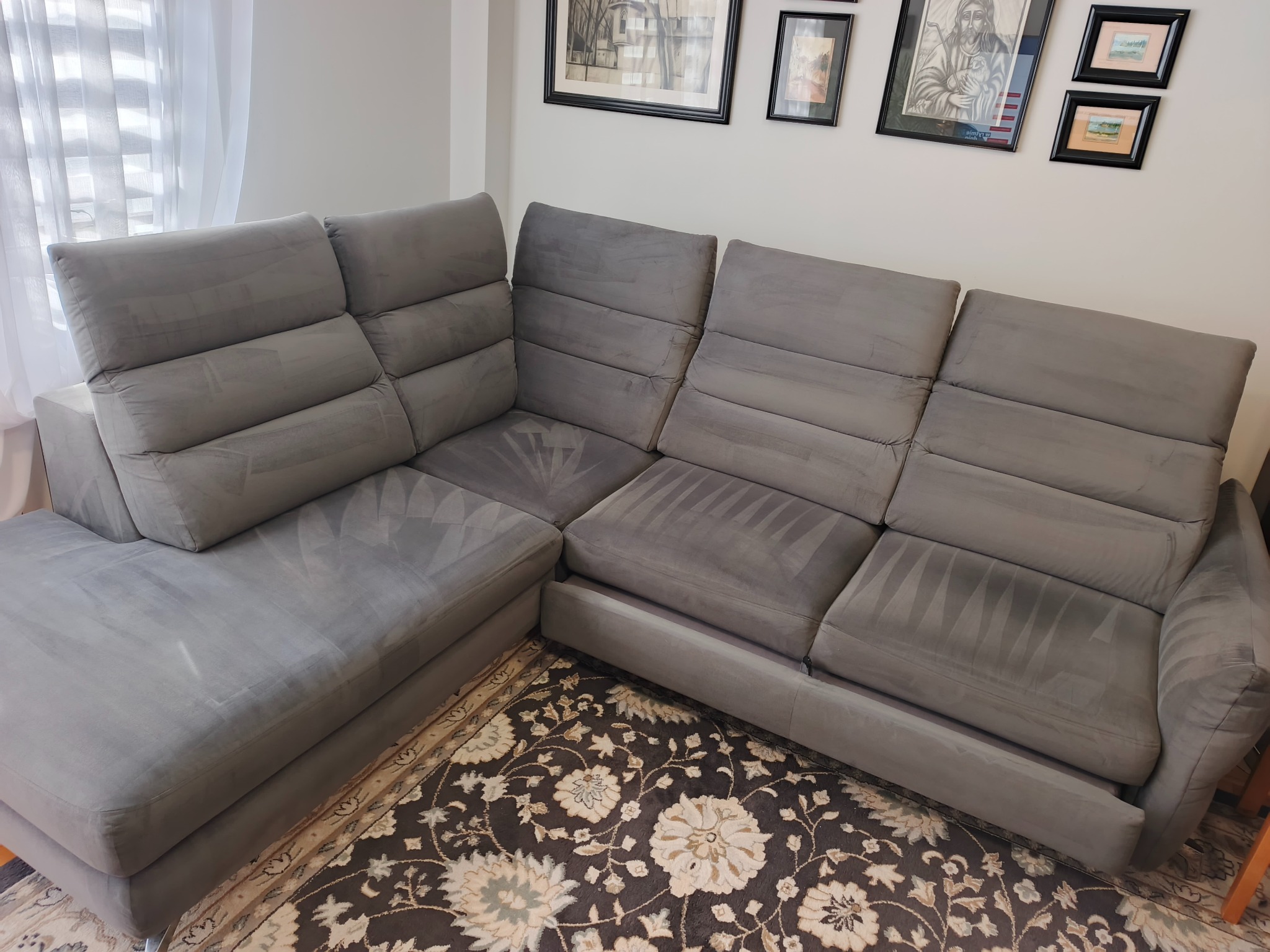 Szara, modułowa kanapa narożna po praniu tapicerki, widoczne ślady po czyszczeniu ekstrakcyjnym. Dywan w kwiaty, obrazy na ścianie w tle.