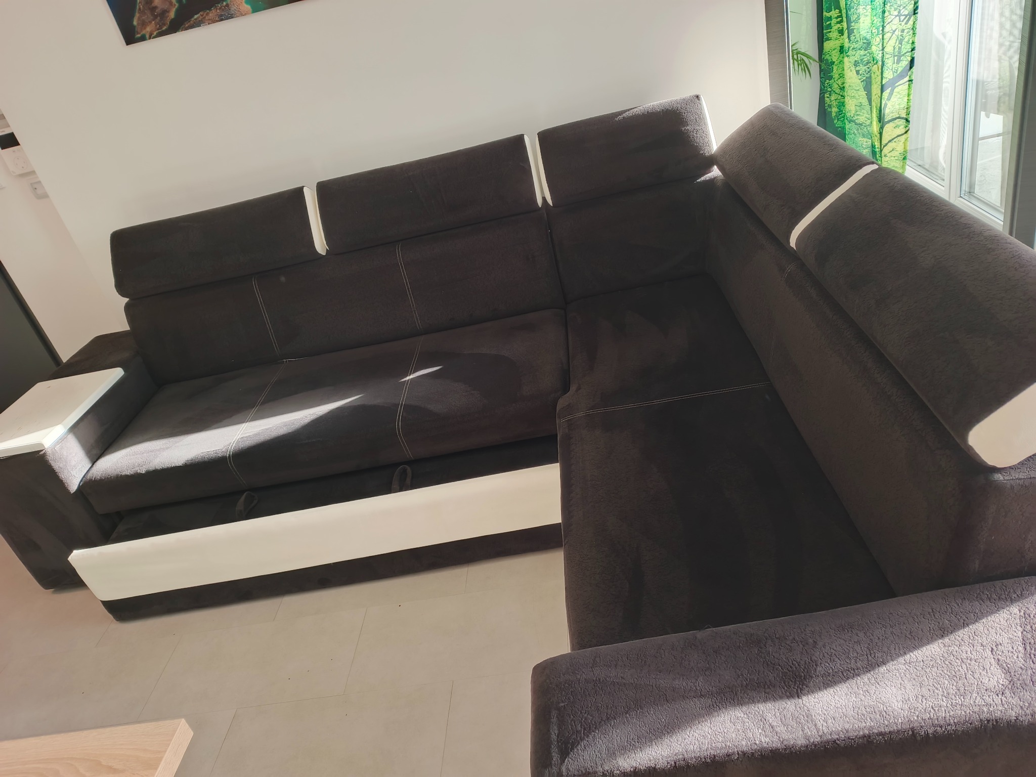 Ciemnobrązowy narożnik z białymi akcentami, widoczny z góry, z rozłożoną częścią do spania. Nowoczesny design, jasne wnętrze, światło słoneczne.