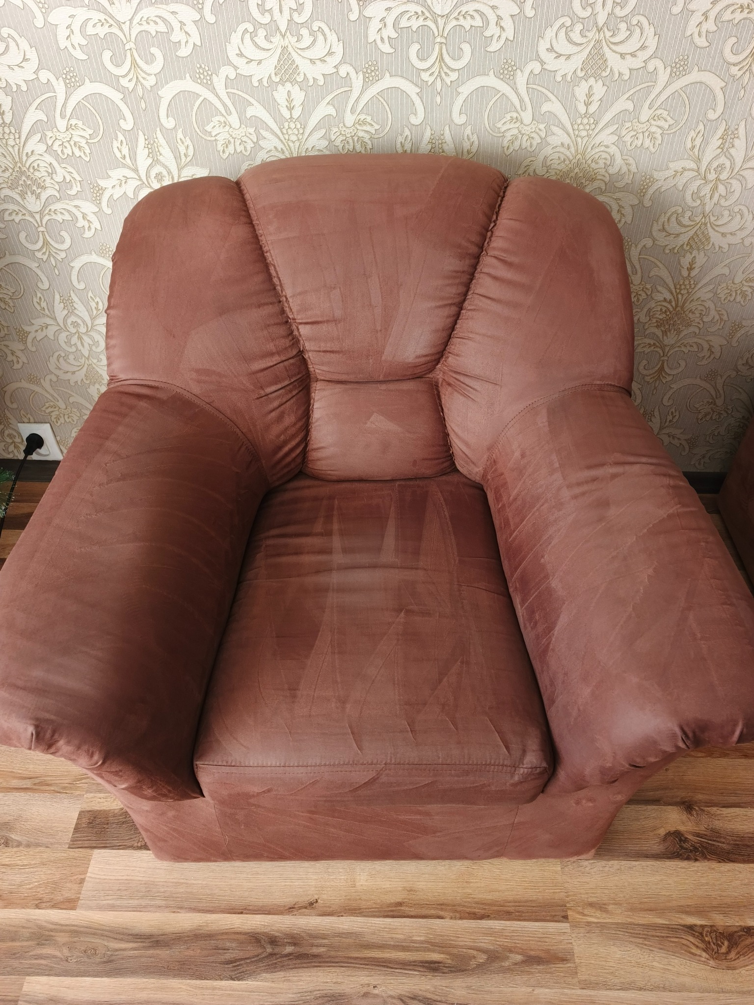Brązowy, pluszowy fotel po praniu tapicerki, widoczne jaśniejsze smugi po czyszczeniu. Na podłodze panele, w tle ściana z wzorzystą tapetą.