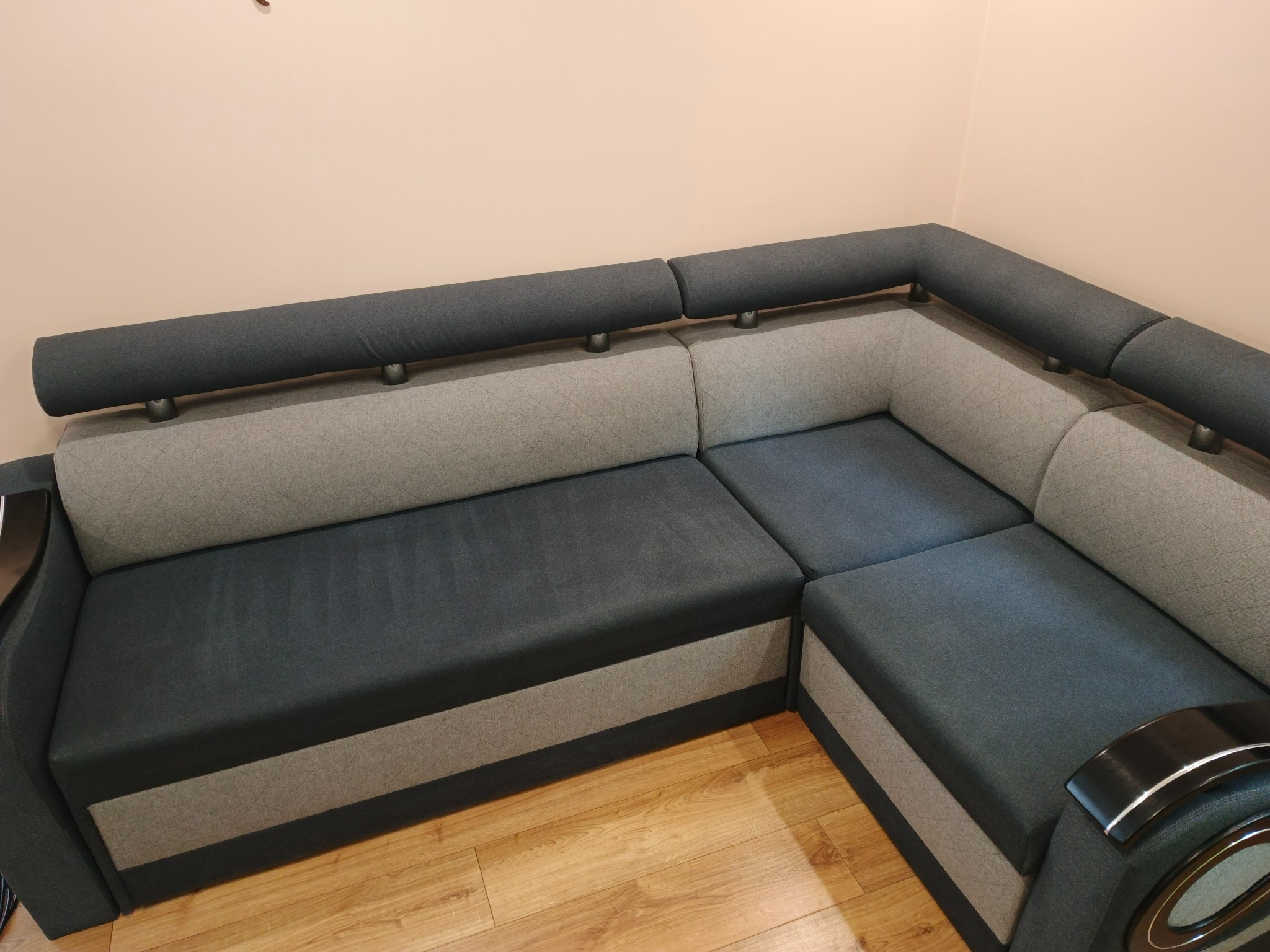 Szaro-grafitowa narożna kanapa z drewnianą podłogą w tle. Widoczne segmenty oparcia i siedziska. Ujęcie z niskiego kąta, podkreślające fakturę materiału.