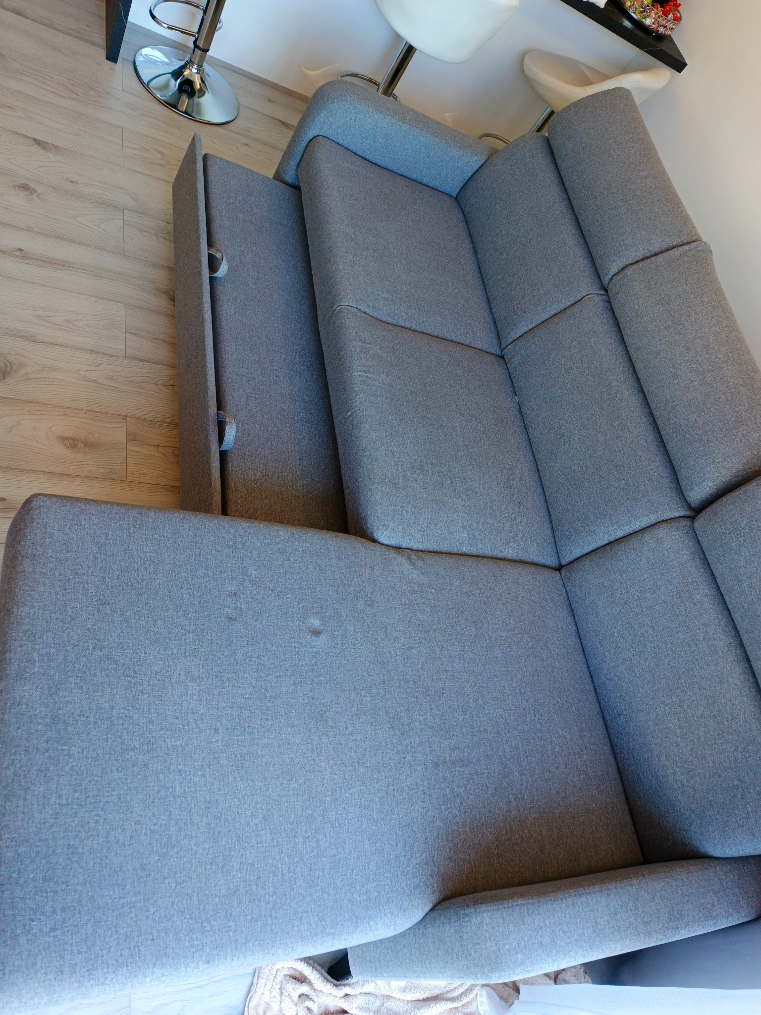 Szara, rozłożona kanapa narożna z widocznymi plamami na siedzisku, sfotografowana z góry w Brzeźnicy. Widoczne elementy wystroju wnętrza.