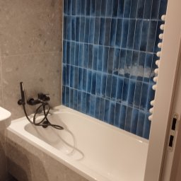 Siergiej Garamiew - Wykończona łazienka z białą wanną, czarną armaturą i ścianą w niebieskich, pionowych płytkach. Widoczne narzędzia na podłodze.