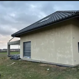 Elewacja domu jednorodzinnego w trakcie prac wykończeniowych; widoczne szpachlowane ściany zewnętrzne i przygotowania do dalszych prac.