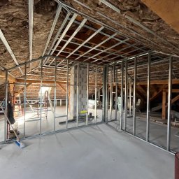 Jakub Owczarek Usługi Budowlane - Montaż metalowej konstrukcji ścian działowych na poddaszu z ociepleniem wełną mineralną. Widoczne profile, bloczki i narzędzia. Etap prac wykończeniowych.