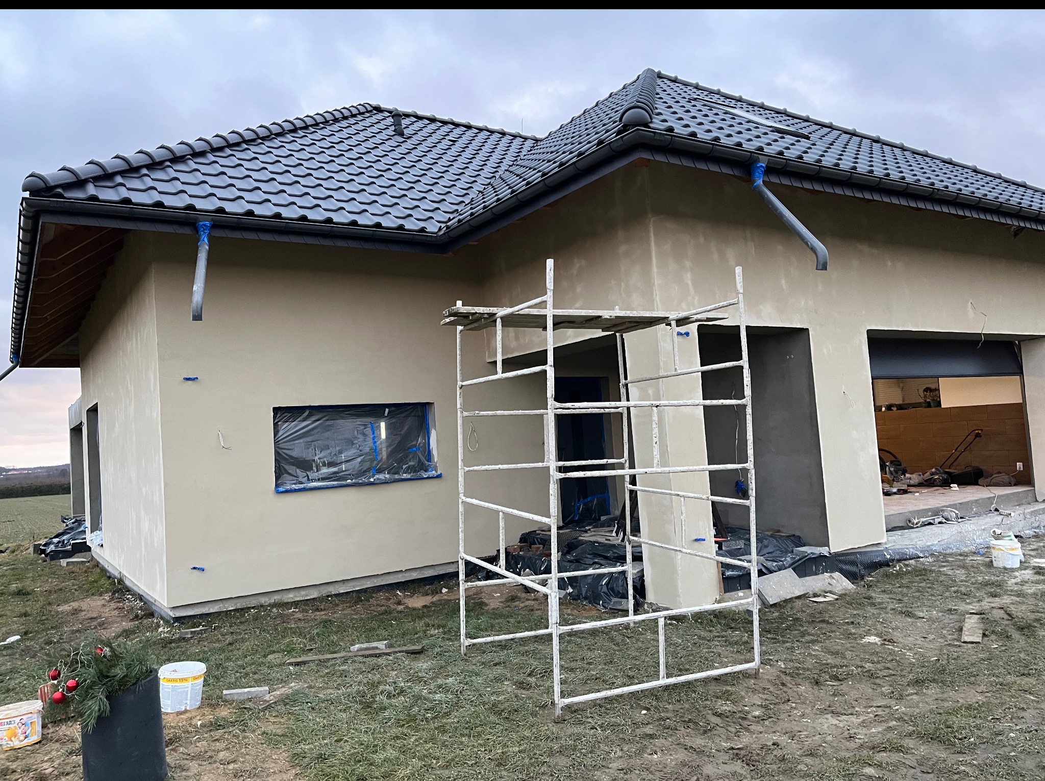 Dom jednorodzinny w trakcie prac wykończeniowych elewacji. Widoczne rusztowanie i zabezpieczone okna folią.