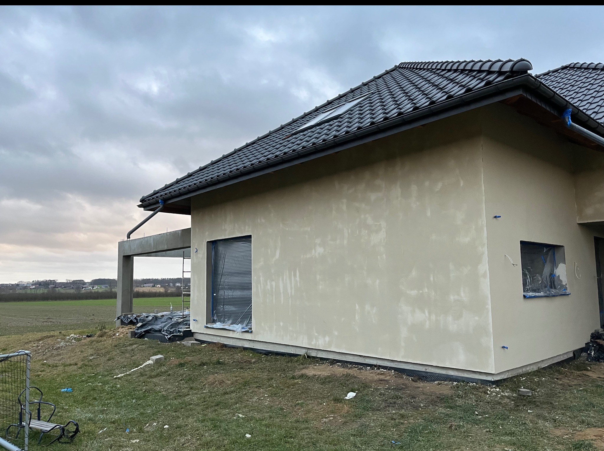 Elewacja domu jednorodzinnego w trakcie prac wykończeniowych; widoczne szpachlowane ściany zewnętrzne i przygotowania do dalszych prac.