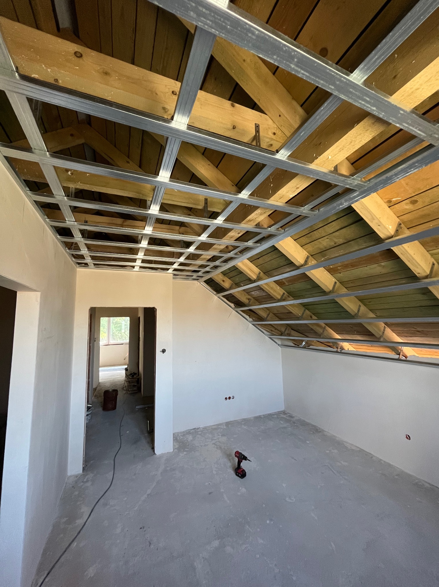 Montaż stelaża sufitu podwieszanego z płyt karton-gips w pomieszczeniu ze świeżo wygładzonymi ścianami. Widoczna wkrętarka na podłodze.