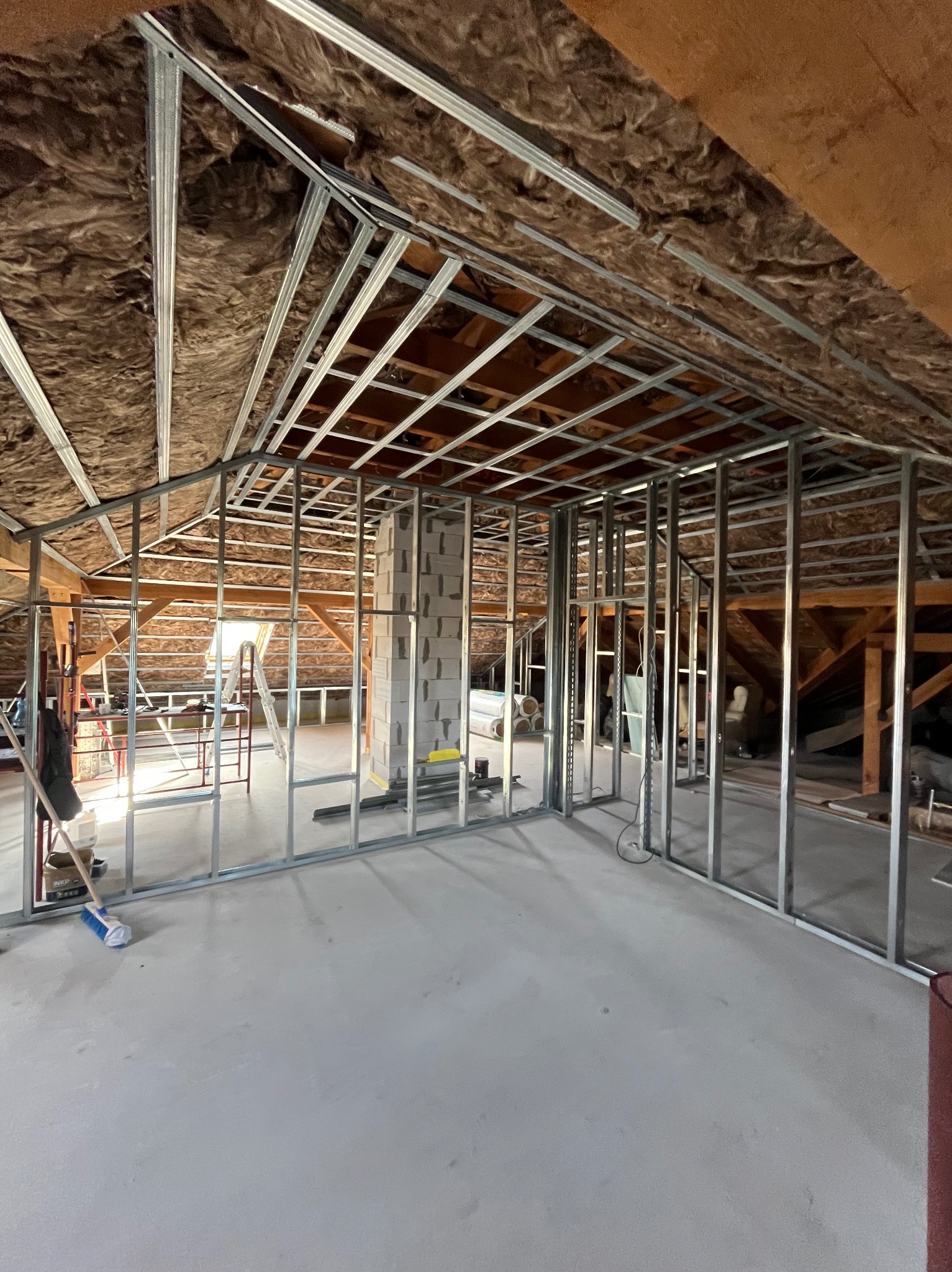 Montaż metalowej konstrukcji ścian działowych na poddaszu z ociepleniem wełną mineralną. Widoczne profile, bloczki i narzędzia. Etap prac wykończeniowych.