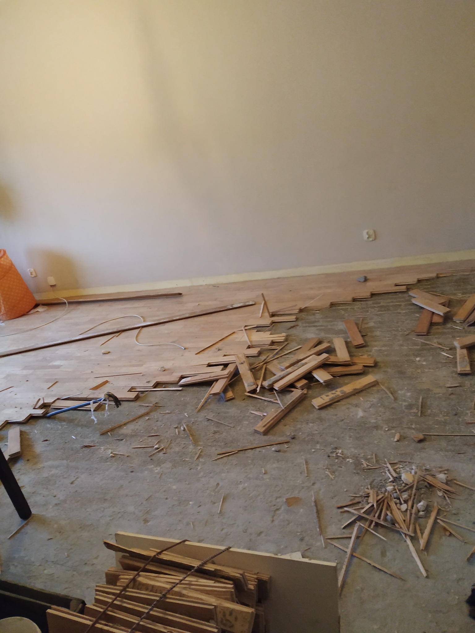 Fragment podłogi w trakcie układania parkietu. Widoczne deski parkietu, narzędzia i resztki materiałów. Częściowo ułożony parkiet kontrastuje z surowym podłożem.