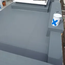 Szary, świeżo pomalowany dach płaski z narzędziami i wiadrem farby. Widok z góry, oświetlenie dzienne.