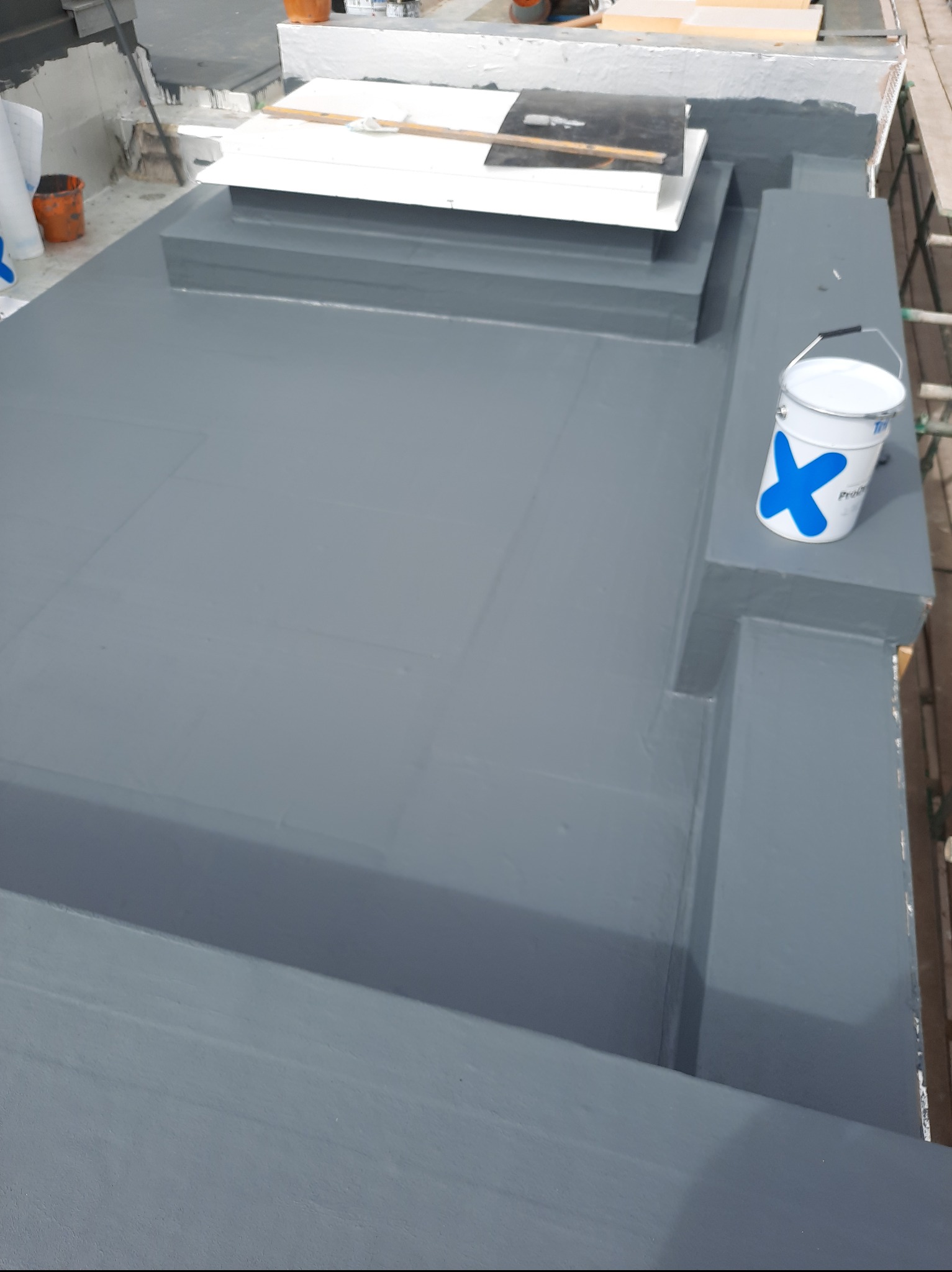 Szary, świeżo pomalowany dach płaski z narzędziami i wiadrem farby. Widok z góry, oświetlenie dzienne.