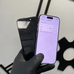 Serwis telefonu: dłoń w czarnej rękawiczce trzyma dwa iPhone'y, jeden z uszkodzonym ekranem, drugi z ekranem po naprawie, z widocznym statusem 'Część oryginalna'.