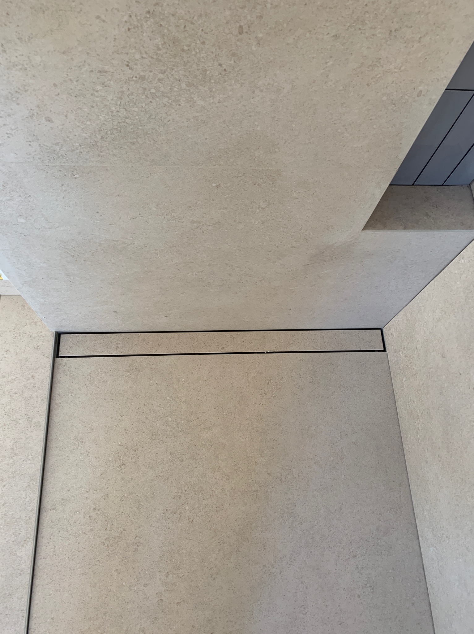 Beżowe płytki podłogowe i ścienne połączone czarnym odpływem liniowym w nowoczesnej łazience, widok z góry.