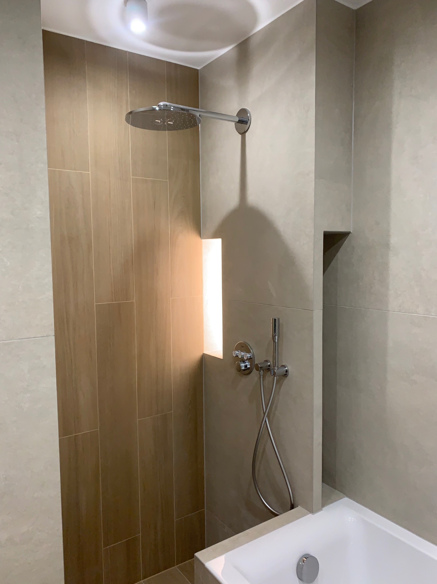 Nowoczesna łazienka z kabiną prysznicową typu walk-in, wykończona płytkami w odcieniach beżu i brązu. Widoczna bateria i deszczownica.