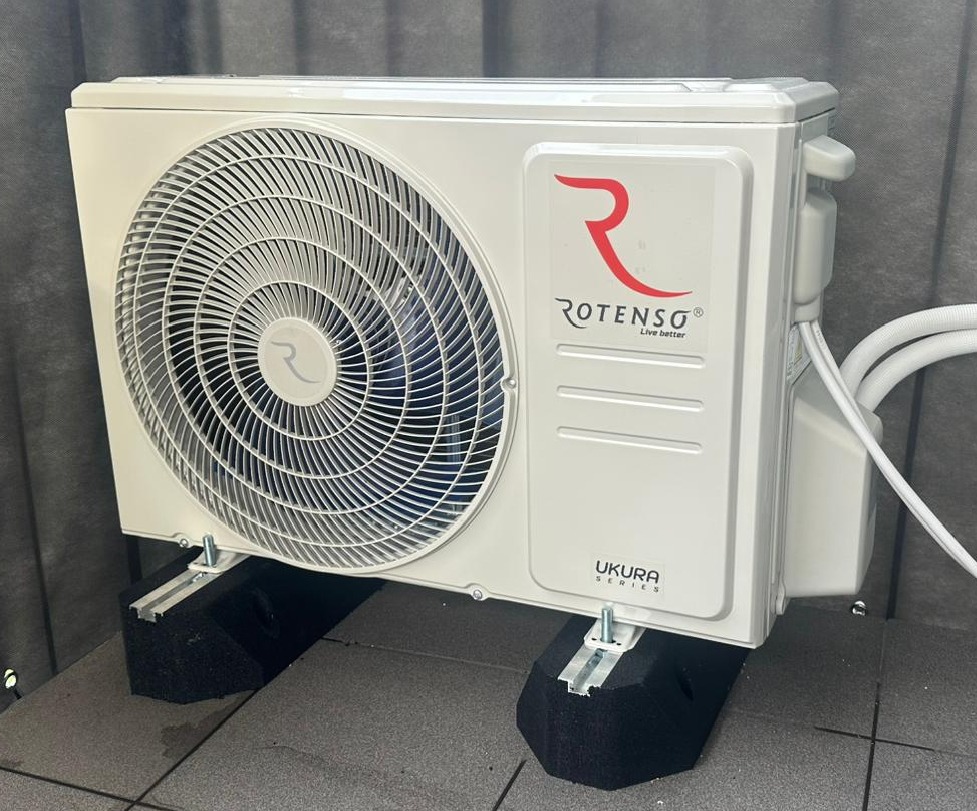 Kompaktowa jednostka zewnętrzna klimatyzacji Rotenso UKURA 3.5 kW, zamontowana na czarnych, dźwiękochłonnych wspornikach, z widocznymi przewodami chłodniczymi.