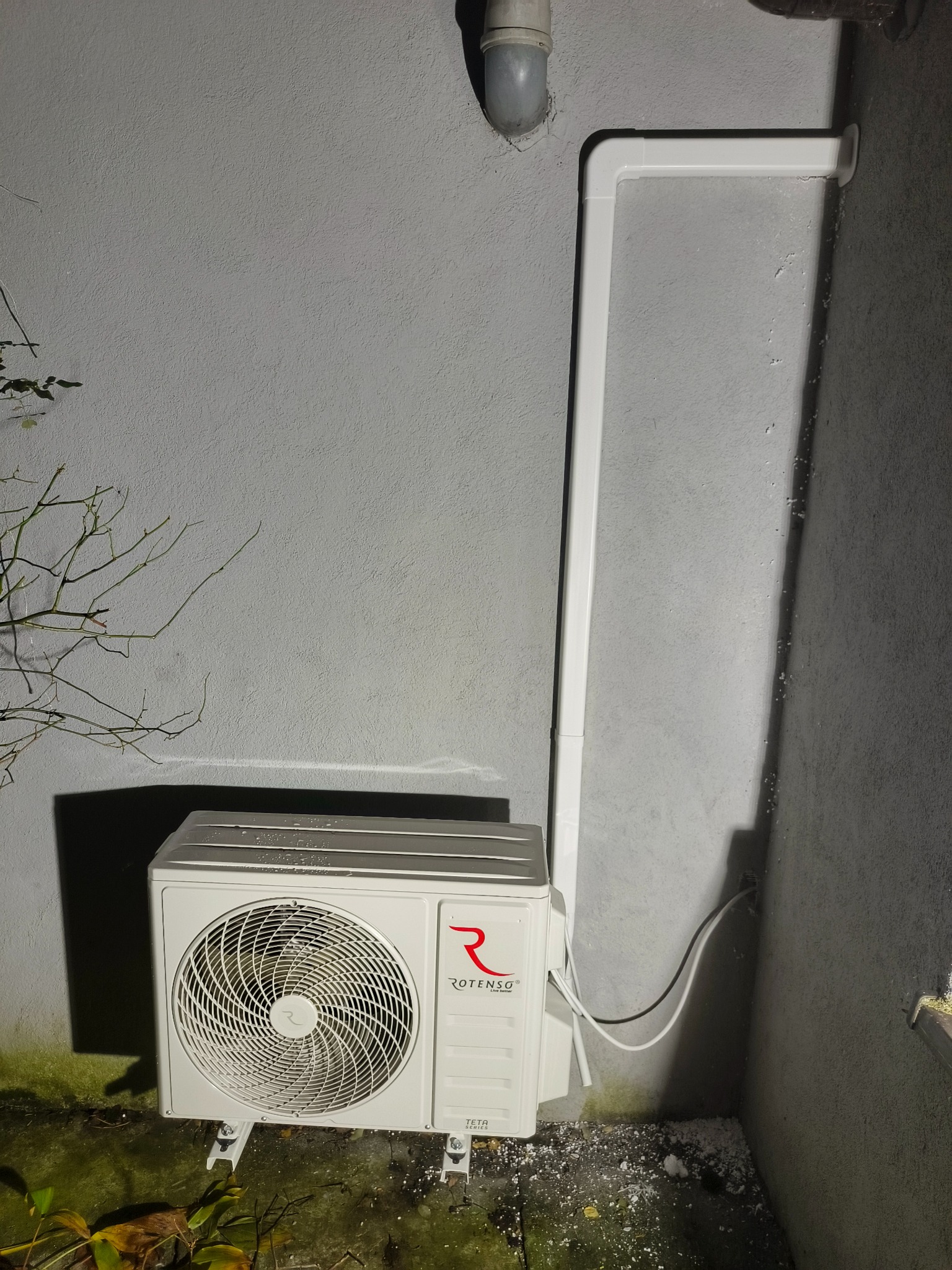Zamontowany klimatyzator Rotenso TETA 2.6 kW na zewnątrz budynku, z widocznymi rurami odprowadzającymi i elementami instalacji na szarej ścianie.