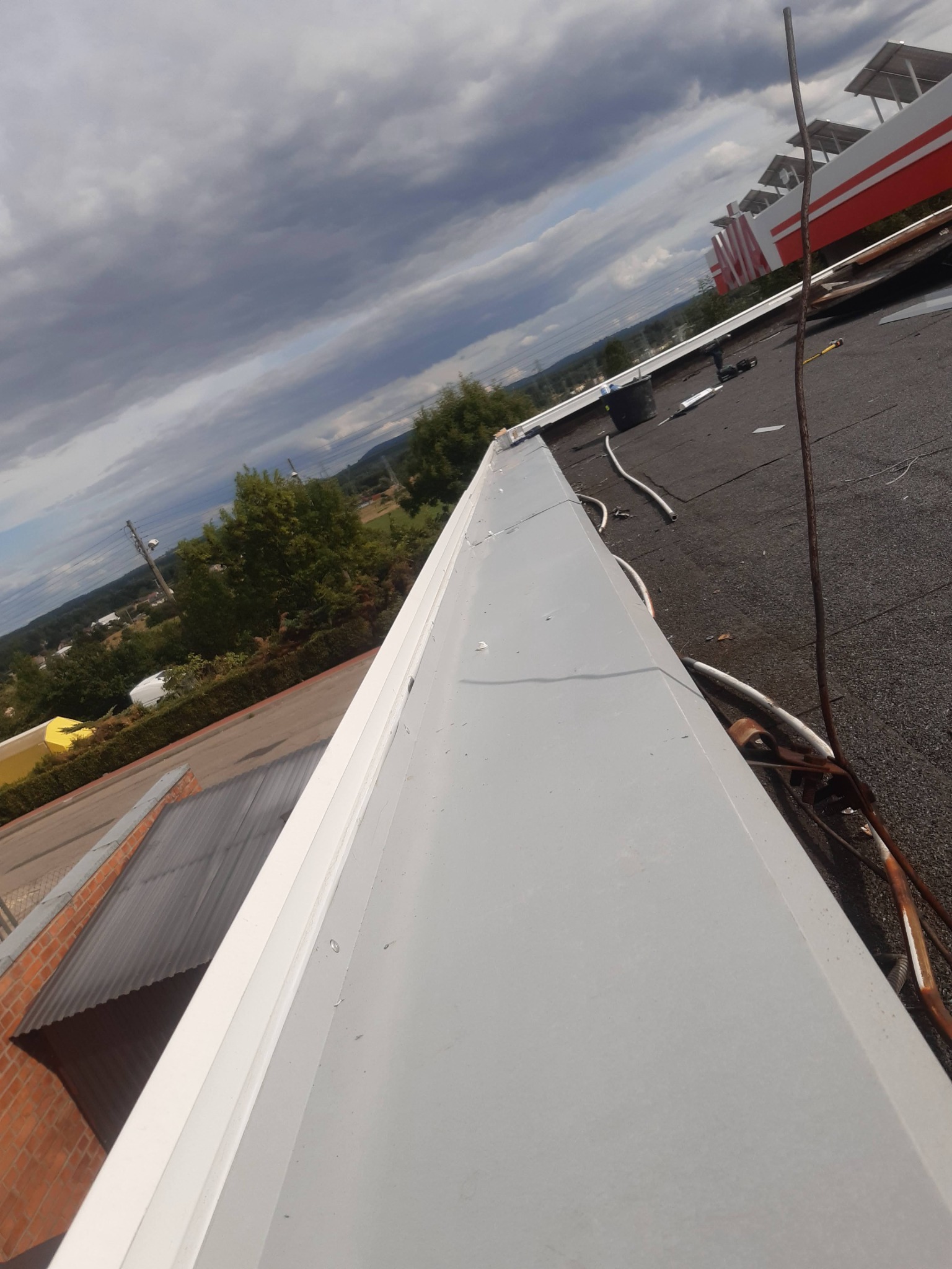 Szara obróbka blacharska na dachu z papy bitumicznej, widok z góry pod kątem. W tle budynki i pochmurne niebo. Elementy instalacji na dachu.