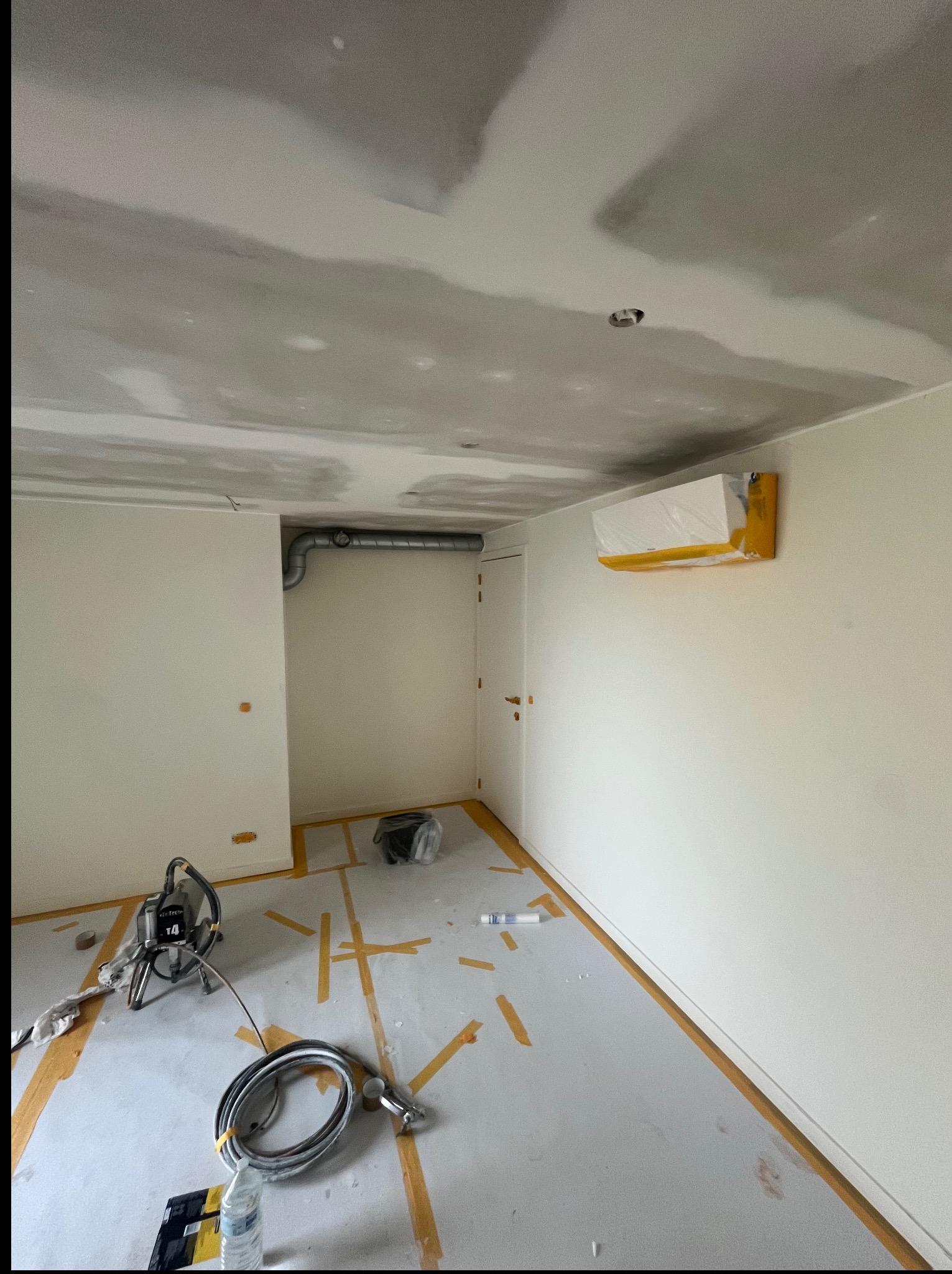 Pokój po szpachlowaniu i malowaniu natryskowym w Gorzowie Wielkopolskim. Zabezpieczone podłogi i klimatyzacja. Widoczny sprzęt do malowania.