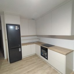 Pracownia Stolarska Hornet - Kamil Żeliszczak - Jasna kuchnia z drewnianym blatem, czarną lodówką i płytą indukcyjną. Minimalistyczny design, proste fronty szafek, nowoczesne oświetlenie. Widok na całą zabudowę kuchenną.