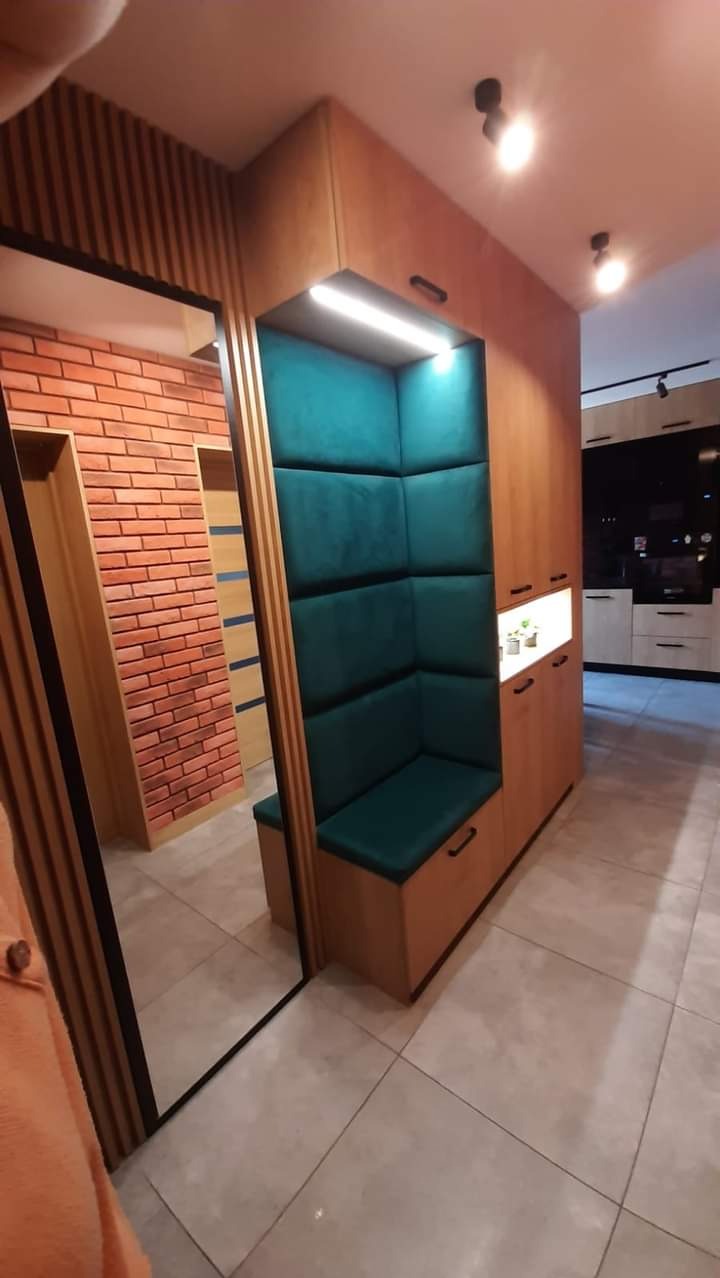 Funkcjonalna szafa wnękowa z siedziskiem obitym zielonym welurem, zintegrowana z lustrem i oświetleniem LED, w tle widoczna zabudowa kuchenna.