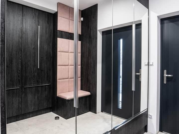 Ciemna szafa wnękowa z siedziskiem obitym różową tkaniną, lustrzane drzwi, nowoczesny design, oświetlenie punktowe, minimalistyczne uchwyty.