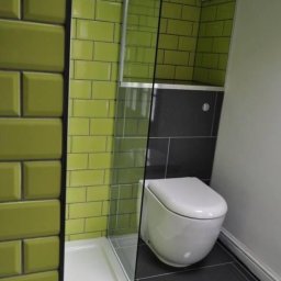 Maciej Sujko - Nowoczesna łazienka z zielonymi płytkami typu metro i czarną strefą WC. Kabina prysznicowa ze szklaną ścianką. Minimalistyczny design z datą na podłodze.