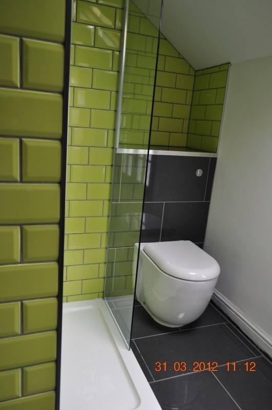 Nowoczesna łazienka z zielonymi płytkami typu metro i czarną strefą WC. Kabina prysznicowa ze szklaną ścianką. Minimalistyczny design z datą na podłodze.