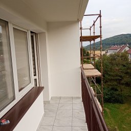 Karol Demko - Balkon po malowaniu z rusztowaniem, widok na zewnątrz. Świeżo pomalowane ściany, płytki na podłodze, brązowy parapet i barierka. Prace wykończeniowe.