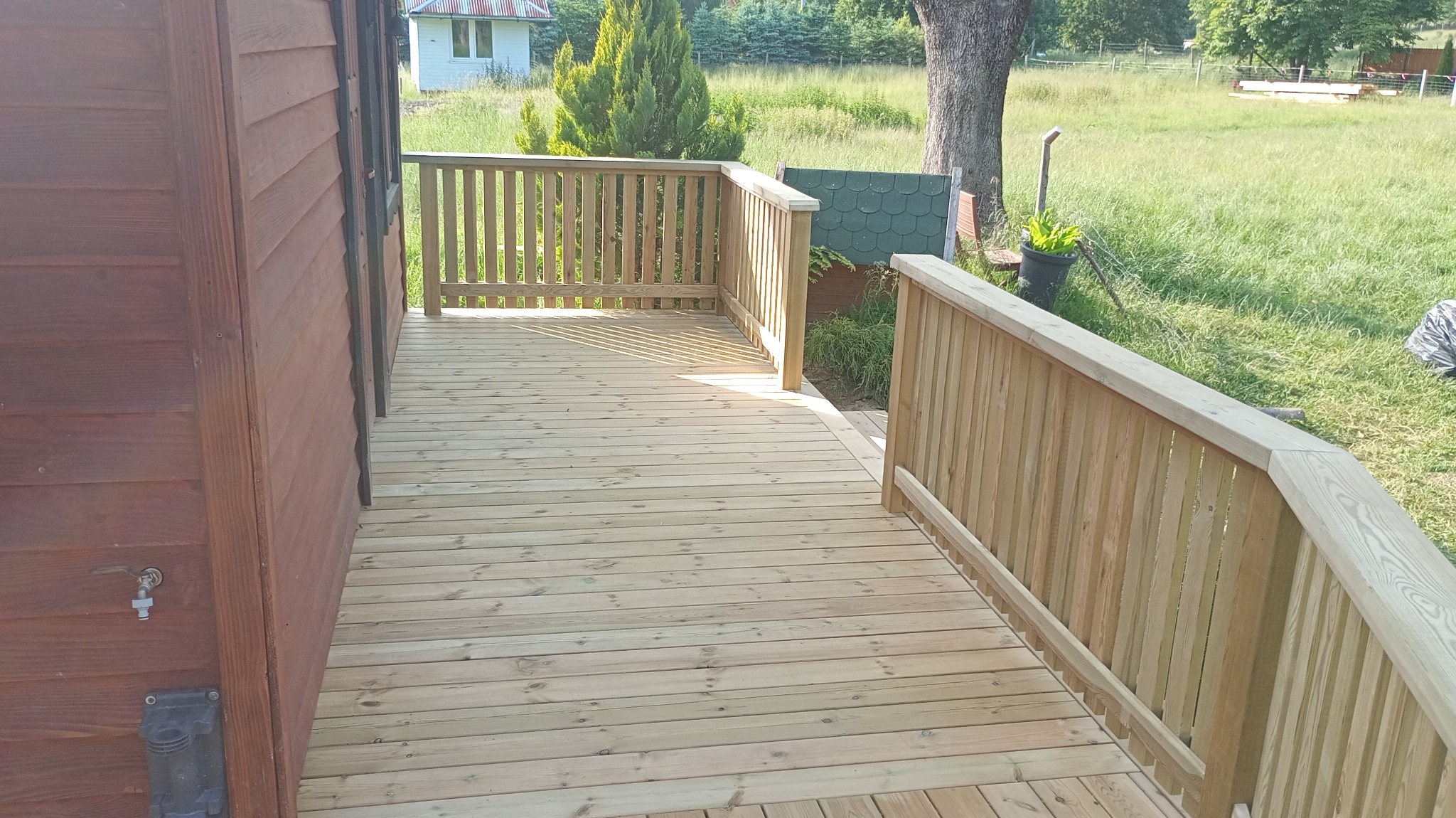 Drewniany taras z balustradą przy domu w Ustrzykach Dolnych. Jasne deski, solidna konstrukcja. Widok na zieleń.