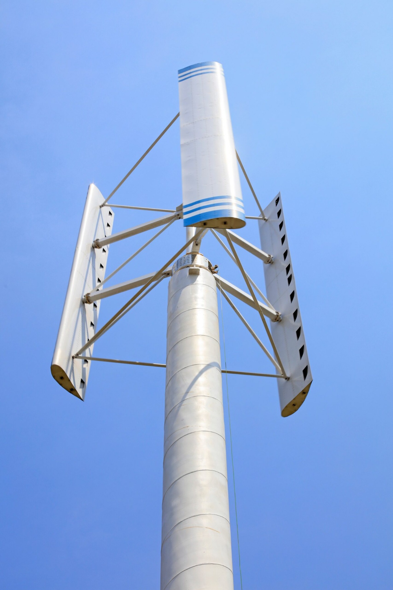 Turbina wiatrowa pionowa z trzema płatami, widok z dołu na tle błękitnego nieba. Płaty w kolorze srebrnym z niebieskimi akcentami.