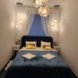 MG PROJEKT GRZEGORZ RADTKE - Klimatyczna sypialnia w Gdańsku po wykończeniu: niebieskie łóżko z weluru, złote poduszki, designerskie lampy wiszące i subtelne zasłony w oknie.