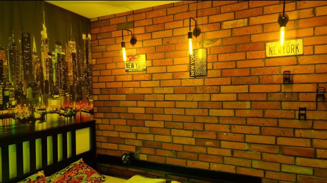 Pokój z ceglaną ścianą, dekoracjami 'New York' i fototapetą z panoramą miasta. Oświetlenie punktowe nadaje wnętrzu loftowy charakter.