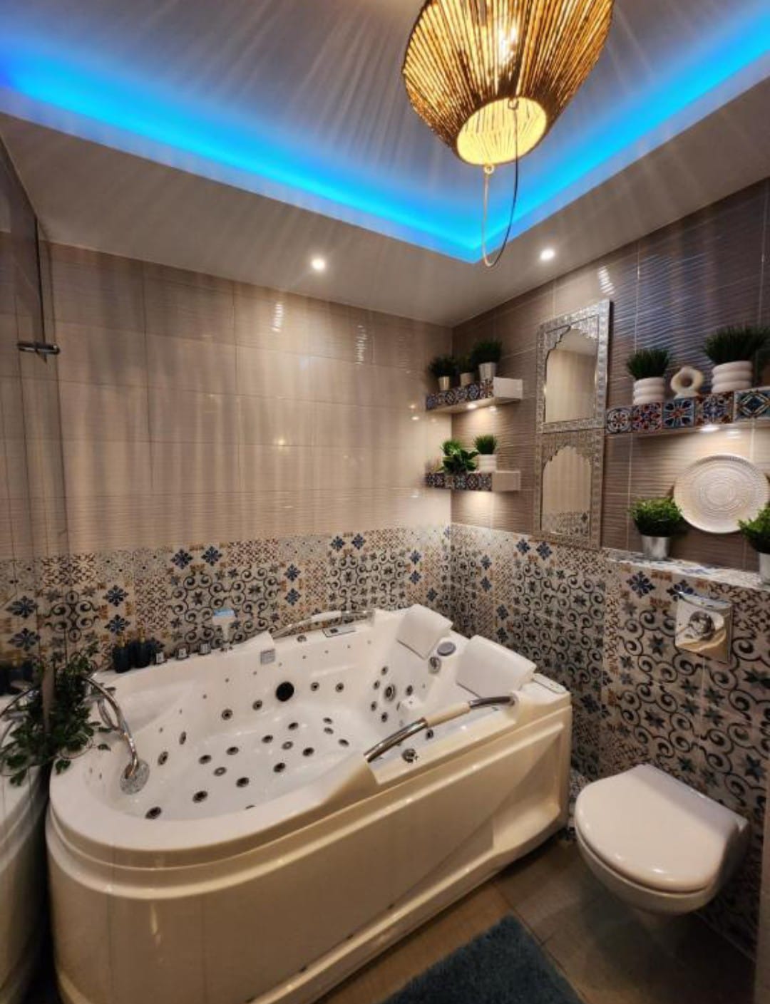 Nowoczesna łazienka z wanną jacuzzi, mozaikowymi płytkami i oświetleniem LED. Dekoracyjne półki z roślinami dodają uroku.