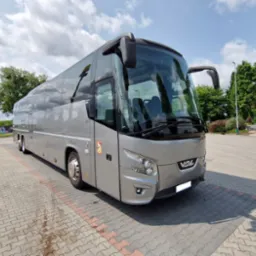 Srebrny autokar VDL na parkingu z kostki brukowej, widok z przodu, błękitne niebo z chmurami w tle. Pojazd po serwisie blacharsko-lakierniczym.