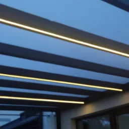 Oświetlenie LED na zewnątrz budynku, zamontowane pod zadaszeniem, widok od dołu. Ciepłe światło podkreśla architekturę.