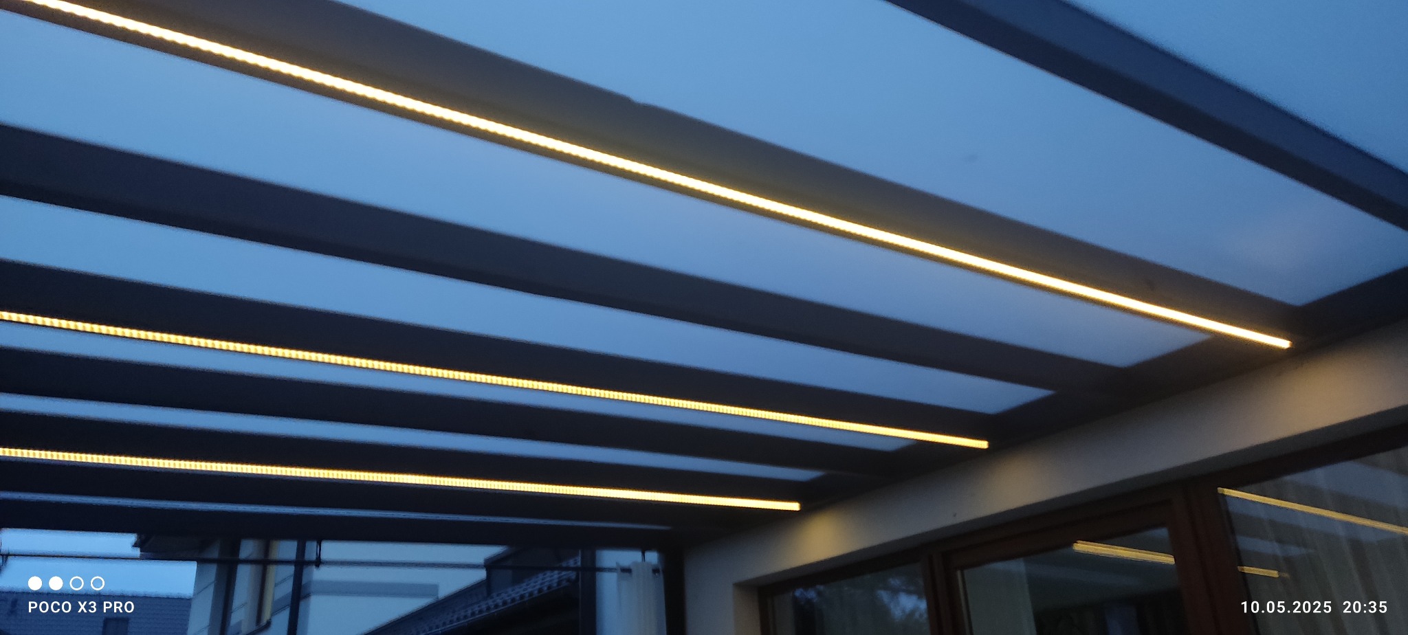 Oświetlenie LED na zewnątrz budynku, zamontowane pod zadaszeniem, widok od dołu. Ciepłe światło podkreśla architekturę.