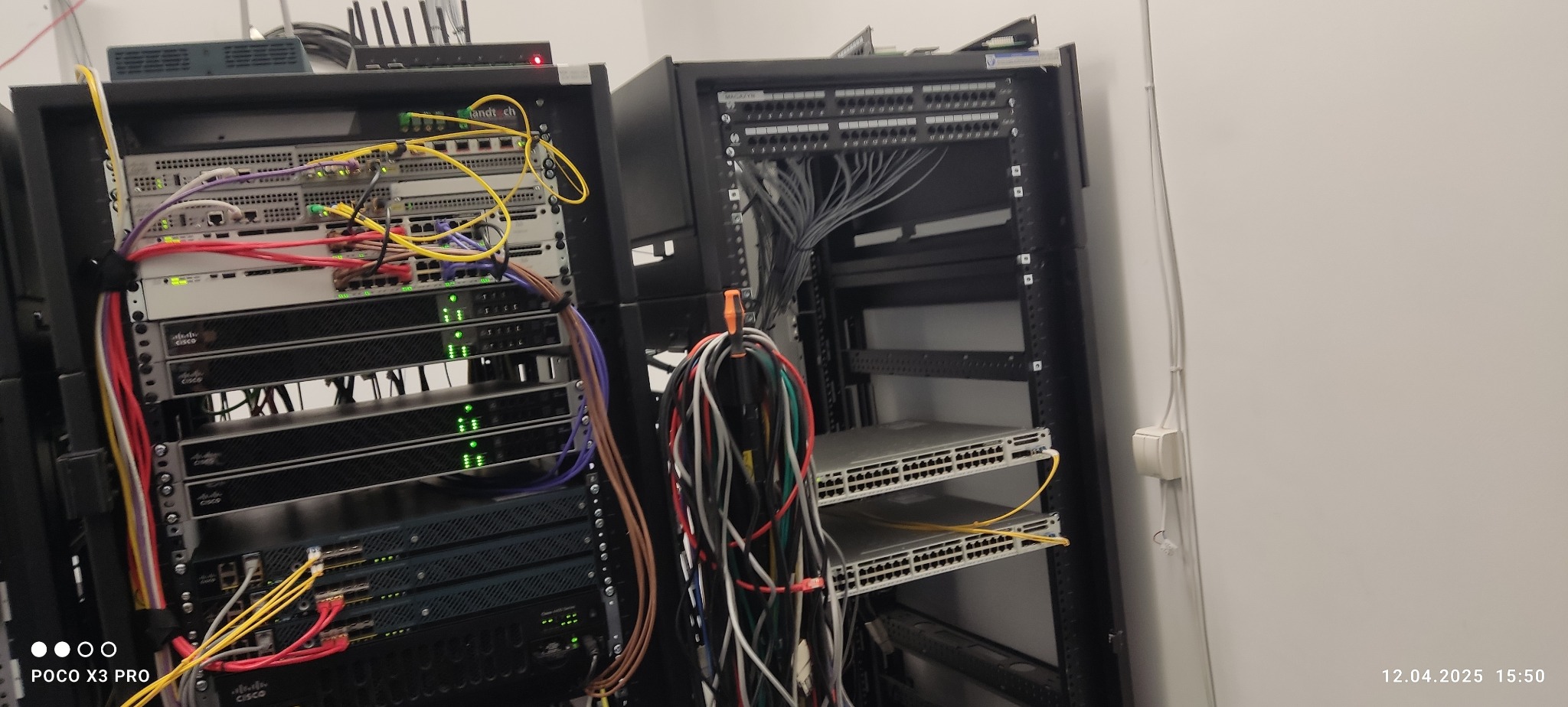 Dwie szafy rack z zamontowanymi urządzeniami sieciowymi Cisco, patch panele i okablowanie. Widoczne porty światłowodowe, kable ethernetowe i zasilające.
