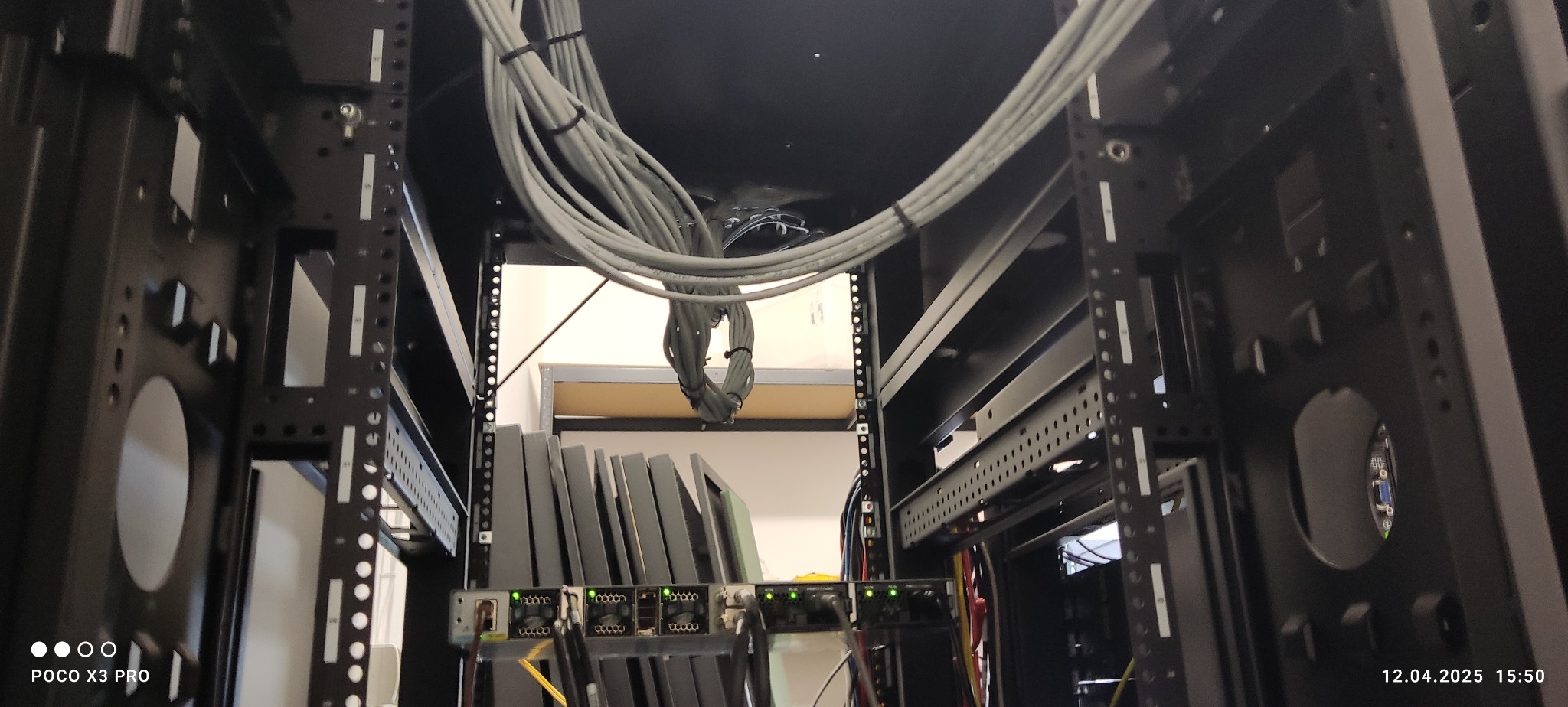 Wnętrze szafy serwerowej z uporządkowanymi kablami i zamontowanym sprzętem. Widoczne kable spięte opaskami i urządzenia sieciowe z diodami sygnalizacyjnymi.