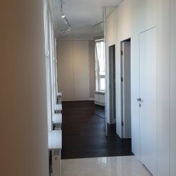 JAKUB SZELĄG PROJEKTOWANIE WNĘTRZ - Nowoczesny korytarz z białymi szafami w zabudowie, lustrami i punktowym oświetleniem. Podłoga z jasnego marmuru przechodzi w ciemne drewno.