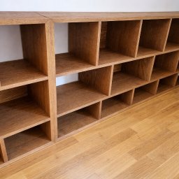 Lignum Art MP corp sp. z o.o. - Regał z jasnego drewna z licznymi przegródkami, ustawiony na podłodze z paneli. Widoczne połączenie dwóch segmentów regału. Minimalistyczny design.