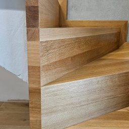 Lignum Art MP corp sp. z o.o. - Fragment nowoczesnych, dębowych schodów z widoczną strukturą drewna, osadzonych na płytkach podłogowych w odcieniach beżu i szarości. Minimalistyczny design.