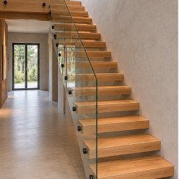 Lignum Art MP corp sp. z o.o. - Nowoczesne schody z jasnego drewna i szklaną balustradą, minimalistyczny design, oświetlenie LED, widok z dołu, perspektywa wnętrza domu.