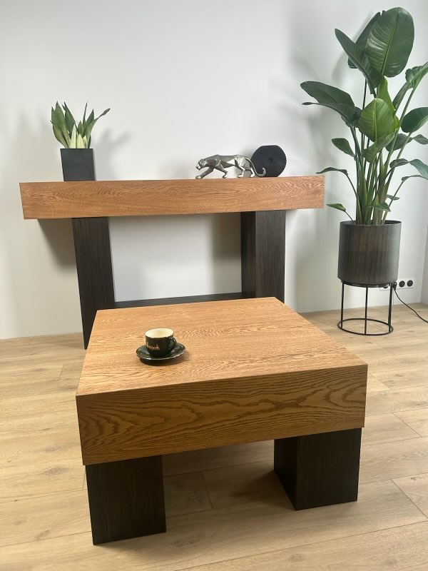 Nowoczesny stolik kawowy z blatem z jasnego drewna i ciemnymi nogami, uzupełniony filiżanką. W tle konsola i roślina doniczkowa, tworzące spójną aranżację wnętrza.