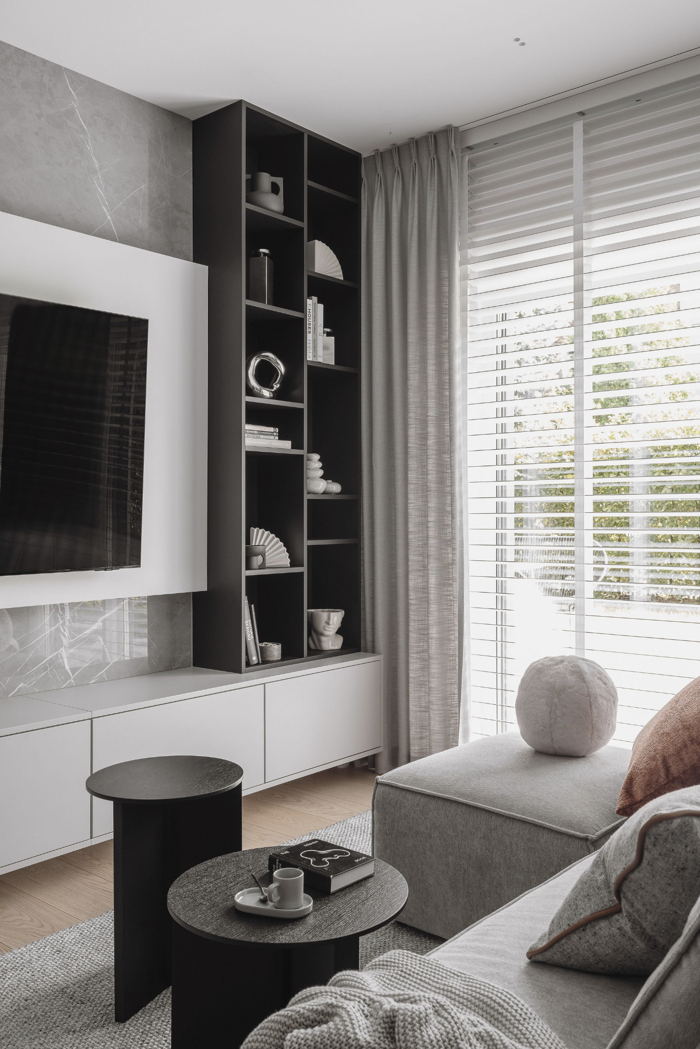 Nowoczesny salon w Poznaniu: szara ściana z marmuru, czarny regał z dekoracjami, stoliki kawowe i wygodna sofa. Minimalistyczny design, jasne wnętrze.