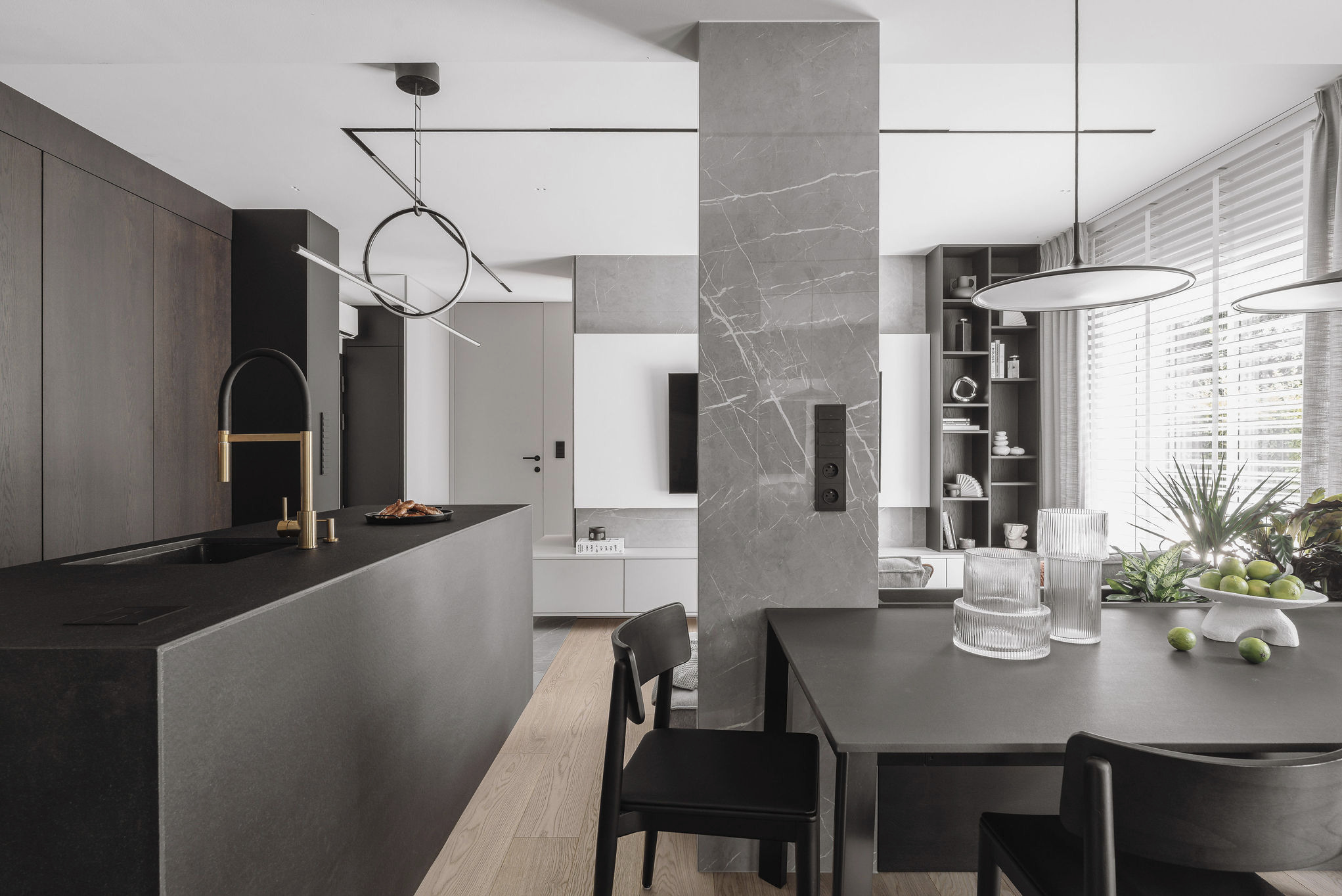 Nowoczesna aranżacja wnętrza: ciemna wyspa kuchenna z złotą armaturą, marmurowy filar, stół z krzesłami i dekoracje, całość w stonowanej palecie barw.